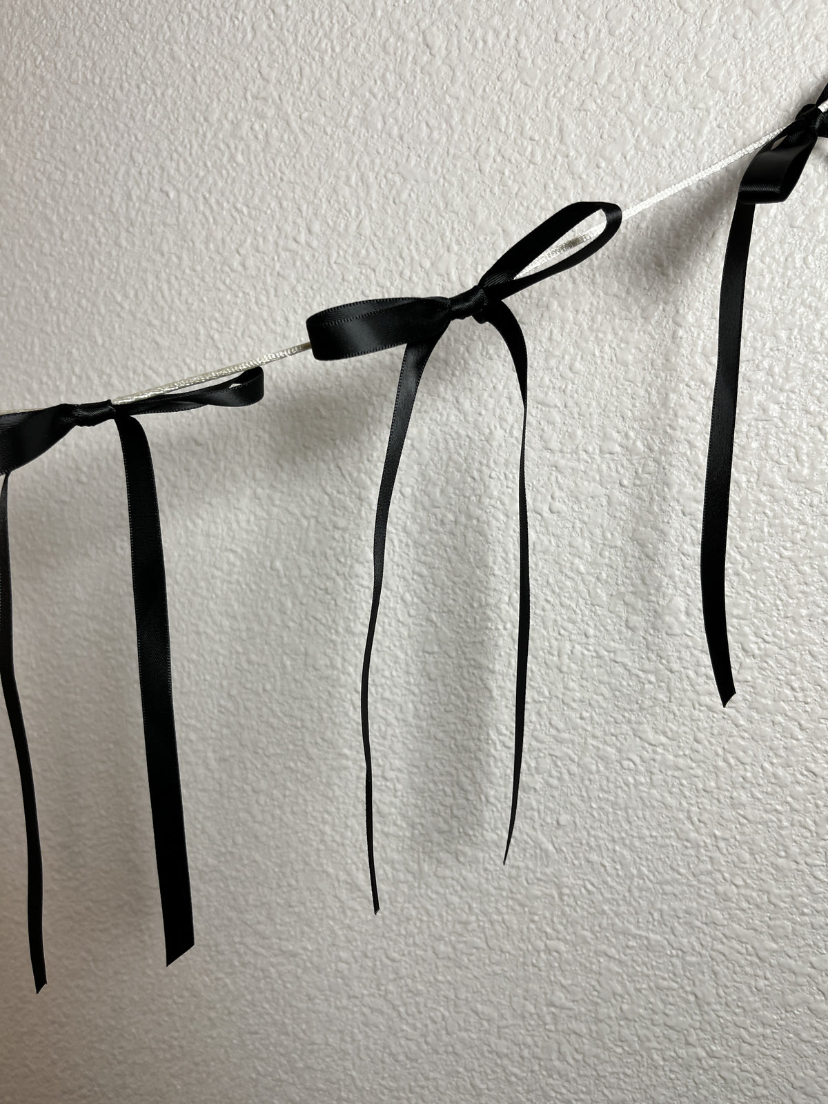 A black satin ribbon garland with tied bows hanging against an off-white wall.