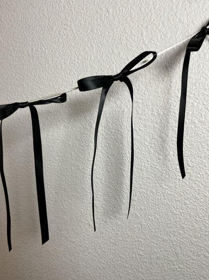 A black satin ribbon garland with tied bows hanging against an off-white wall.